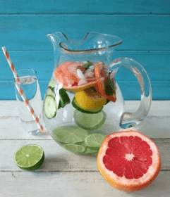 Water pitcher filled with mixed vegitables on a wooden table next to a grapefruit cut in half